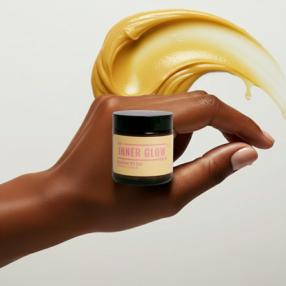 Hand holding a jar of 'Inner Glow' with yellow cream being applied above it on a light background