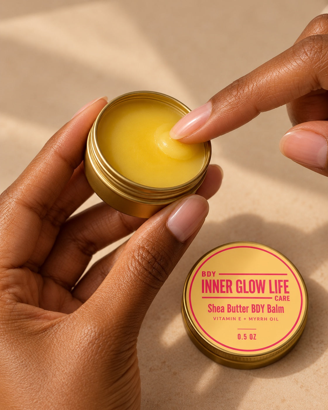 Inner Glow Life Shea Butter BDY Balm 0.5 oz in a gold tin, being applied with a fingertip